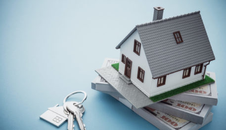 A small model home is sitting on a stack of money with a set of keys showcasing refinancing myths debunked.