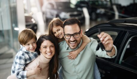 A family is standing in front of their new car showcasing how easy their car loan pre approval was to obtain.
